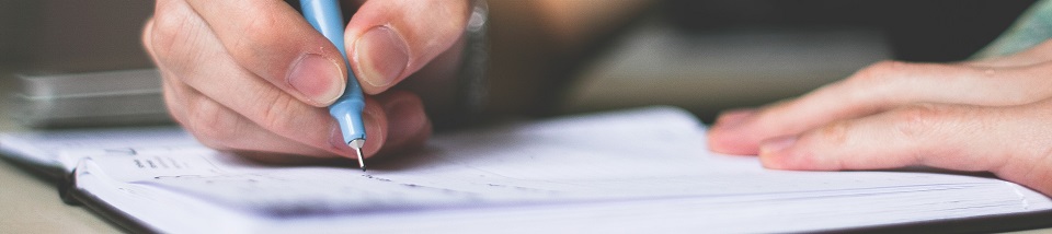 person holding blue ballpoint pen writing in notebook 210661